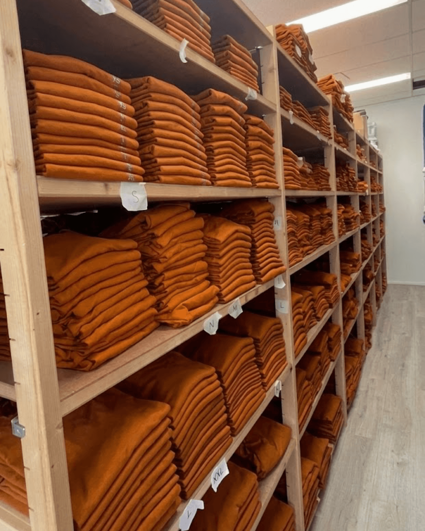 Ons magazijn vol met gevouwen oranje kleding, gesorteerd op maat